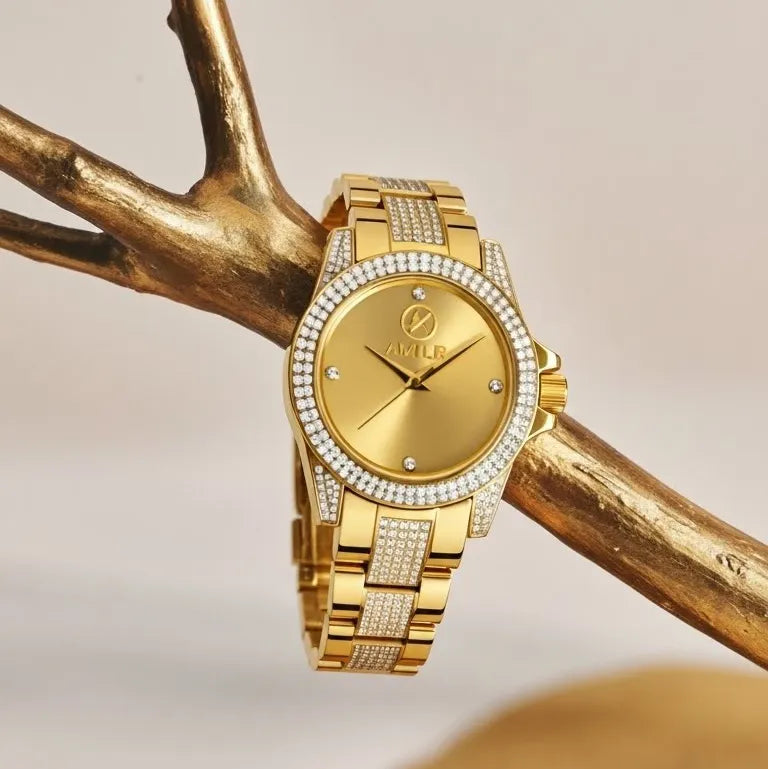 Gold-tone AKLID women's watch with a diamond-encrusted bezel and link bracelet, displayed on a decorative gold branch against a soft beige background.