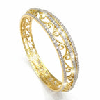 A gold filigree bangle bracelet with two rows of sparkling clear stones, shown on a clean white background.