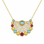 A gold necklace with a semi-circular, tiered pendant featuring a central light blue stone, surrounded by yellow, red, and clear stones, on a plain white background.