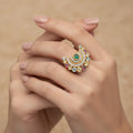 A distinctive ring featuring a beautiful green center stone surrounded by delicate detailing. A graceful statement piece designed to add a touch of color and elegance to your look.