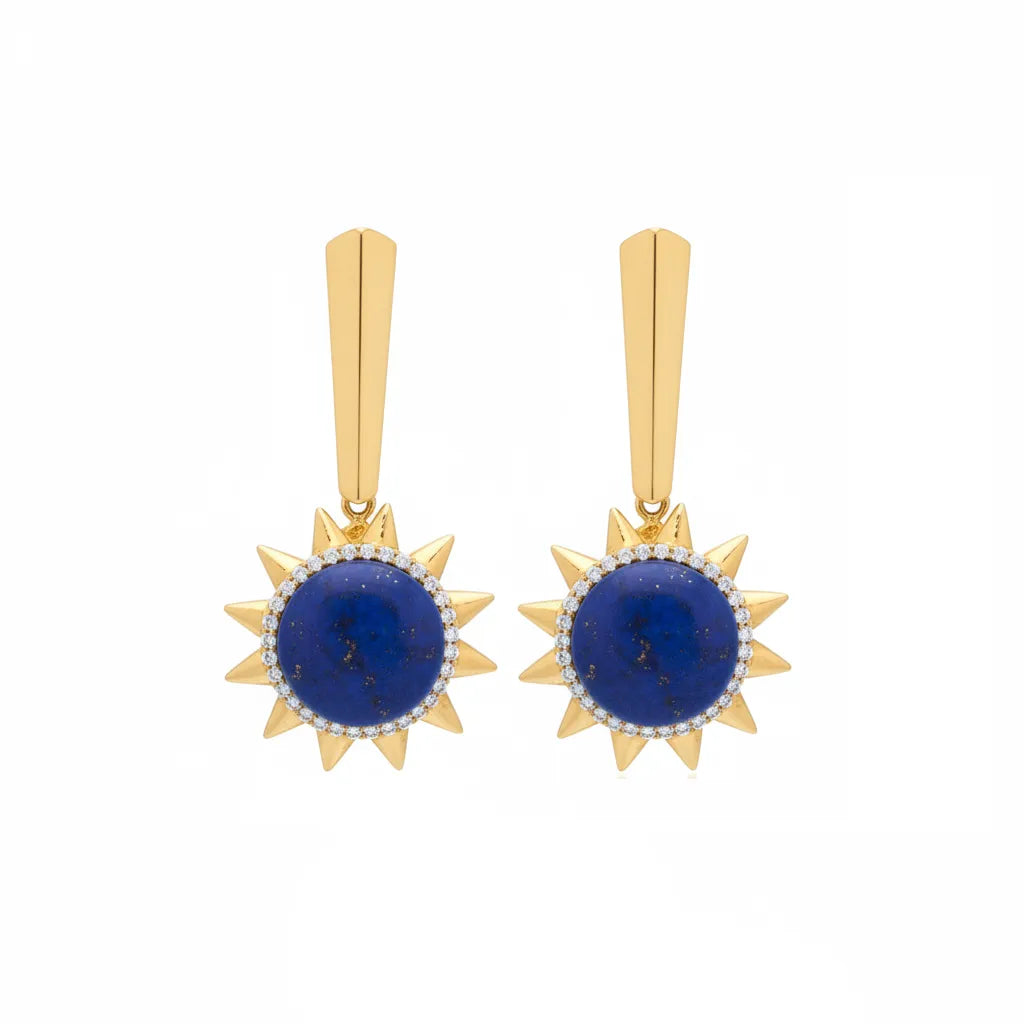A pair of gold drop earrings featuring a central round deep blue lapis lazuli stone surrounded by a halo of small clear pavé stones, with a geometric gold post above, set against a plain white background.