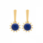 A pair of gold drop earrings featuring a central round deep blue lapis lazuli stone surrounded by a halo of small clear pavé stones, with a geometric gold post above, set against a plain white background.