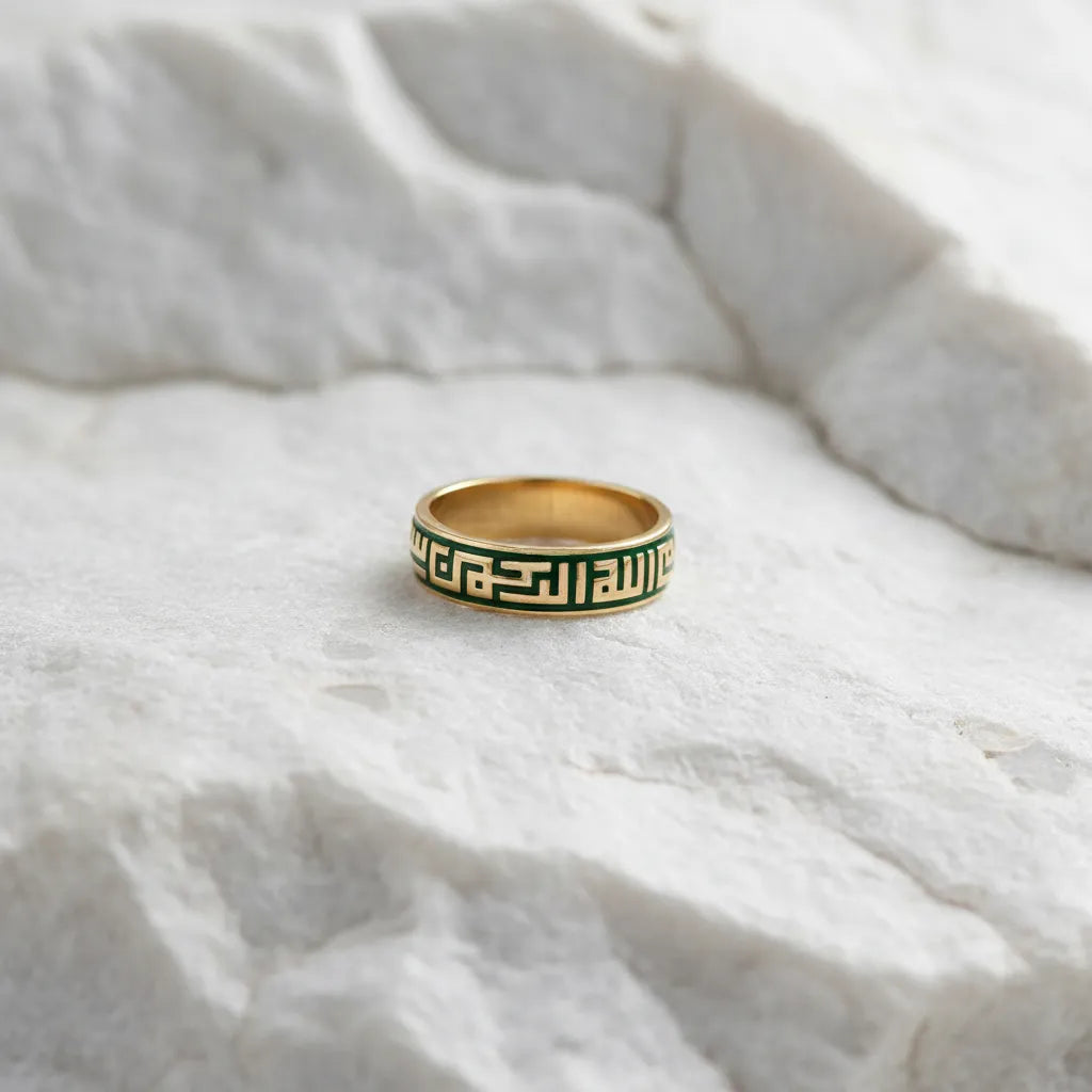 A gold band ring with a green Greek key pattern, resting on a textured white stone surface.