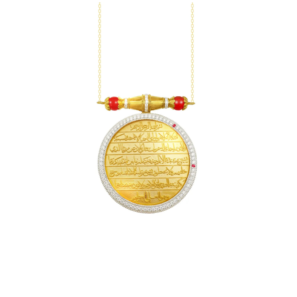 A gold pendant necklace featuring a circular disc engraved with Arabic calligraphy, bordered by pavé-set clear stones, with a gold cylindrical connector and red gemstone accents, suspended from a delicate gold chain on a white background.