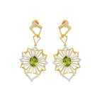 A pair of gold drop earrings with a geometric sunburst design, featuring green peridot gemstones in the center and clear pavé-set stones along the edges, shown on a plain white background.